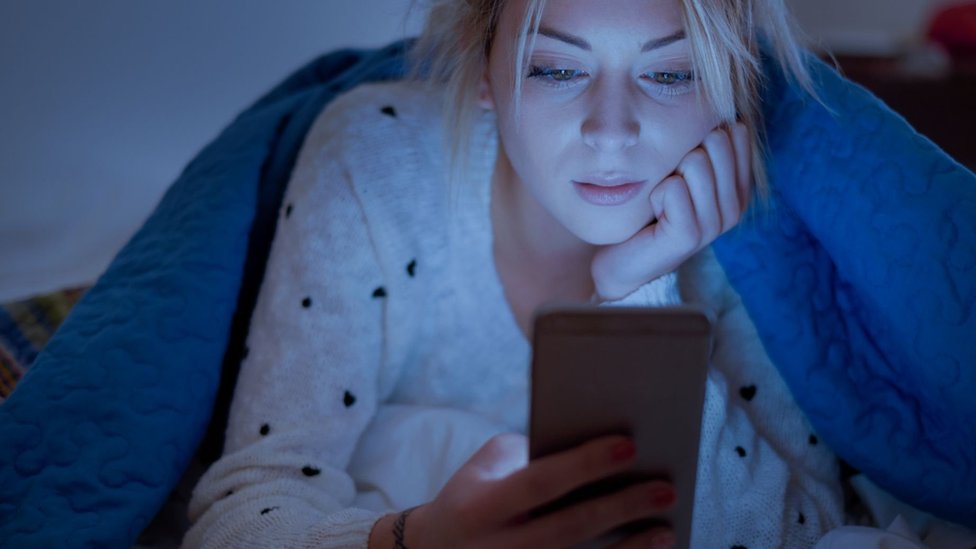 Mujer con celular en la cama.