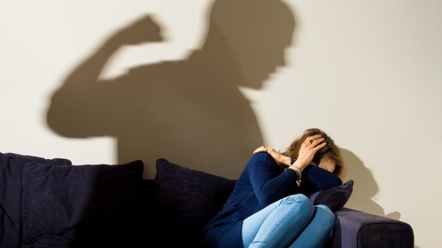 PICTURE POSED BY MODEL A shadow of a man with a clenched fist as a woman cowers in the corner