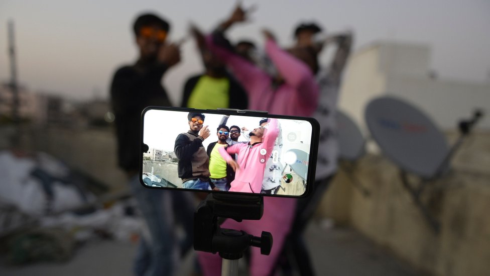 Молодые люди выступают перед камерой мобильного телефона, снимая видео в TikTok на террасе своего дома в Хайдарабаде, февраль 2020 г.