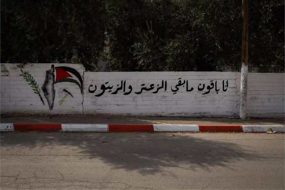 مقولة فلسطينية - "سنبقى هنا ما دام هناك زعتر وزيتون" - على الجدار الذي قُتل فيه معاذ عودة
