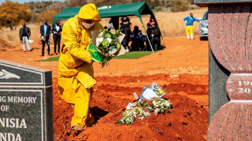 Гробовщик в средствах индивидуальной защиты (СИЗ) возлагает цветы на могилу с останками Модизе Мотлхабане, умершего от коронавируса COVID-19, во время похорон на кладбище Вестпарк в Йоханнесбурге 22 июля 2020 года.