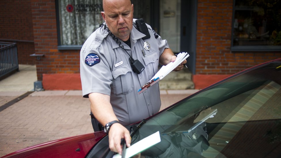 Un policía pone una multa a un auto por estar mal estacionado.