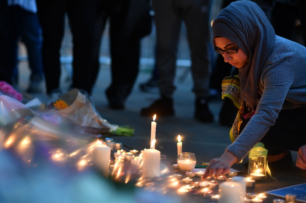 Женщина зажигает свечи перед цветочными площадками на Альберт-сквер в Манчестере