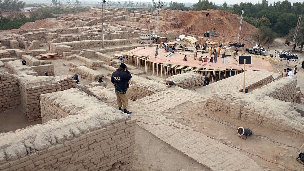 Полицейский наблюдает, как пакистанские рабочие готовят сцену вокруг древних руин перед фестивалем культурного наследия в Мохенджо-Даро, объекте Всемирного наследия ЮНЕСКО, примерно в 425 километрах к северу от портового города Карачи, 30 января 2014 г.