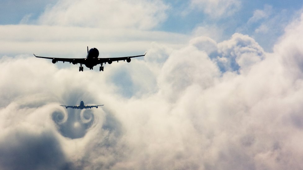 One plane flies through the turbulence in clouds caused by the plane in front