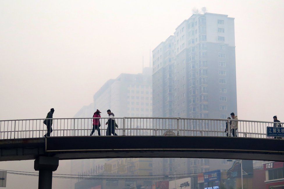 На этом снимке, сделанном 8 ноября 2015 года, изображены жители Китая, идущие по пешеходному мосту в Шэньяне, китайская провинция Ляонин