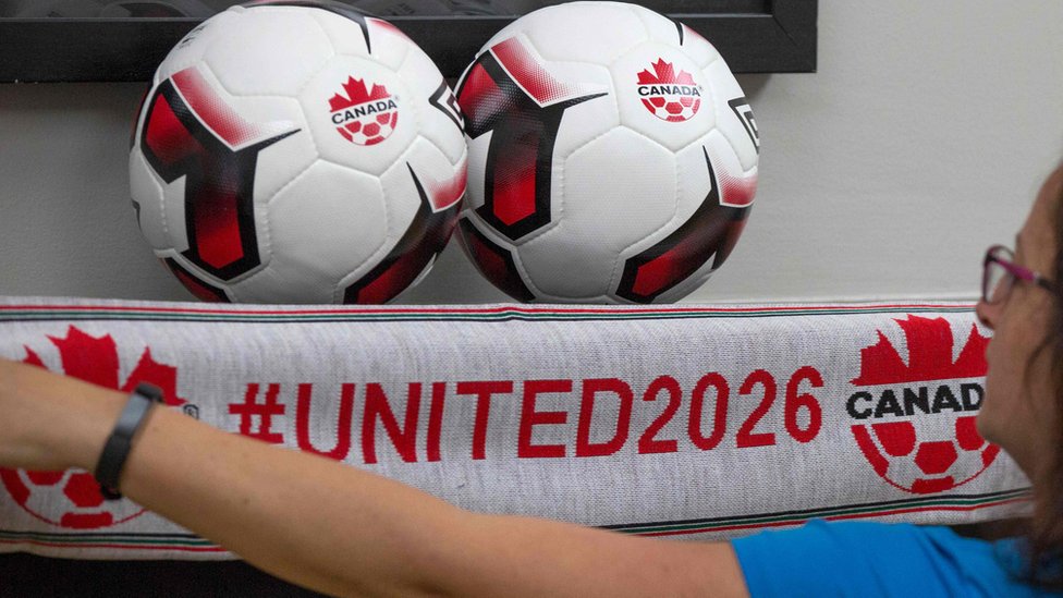 Los promotores estiman en US$11.000 millones los beneficios que dejará el Mundial 2026. Una mujer junto a dos balones y una bufanda de la candidatura de Canadá al Mundial