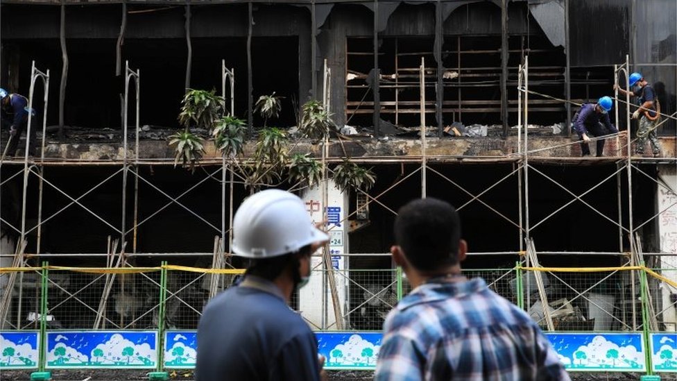Men stand in front of a damaged residential building after a fire as workers build scaffoldings outside, in Kaohsiung, Taiwan October 15, 2021.