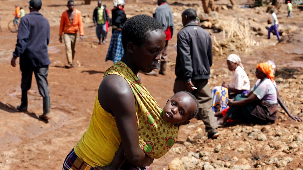 Женщина несет своего ребенка, когда она идет возле разрушенных домов в результате наводнения после прорыва дамбы в городе Солио недалеко от Накуру, Кения, 10 мая 2018 года.
