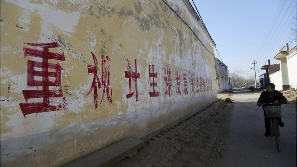 Житель проезжает на велосипеде мимо лозунга на стене, на котором частично написано «Обратите внимание на политику в отношении одного ребенка и ищите возможности для развития», в деревне в Ханьдане, провинция Хэбэй, Китай, декабрь 2014 г.