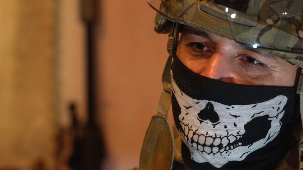 Sniping team commander, Ghost, is pictured wearing a military helmet with a mask featuring a skull design covering his mouth and nose