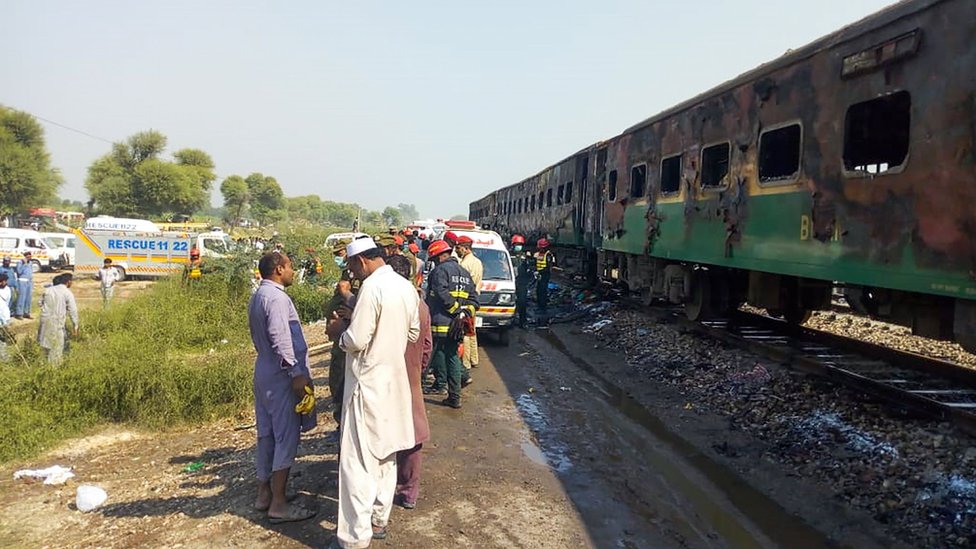 Authorities stand by the charred wreckage of the train in Pakistan