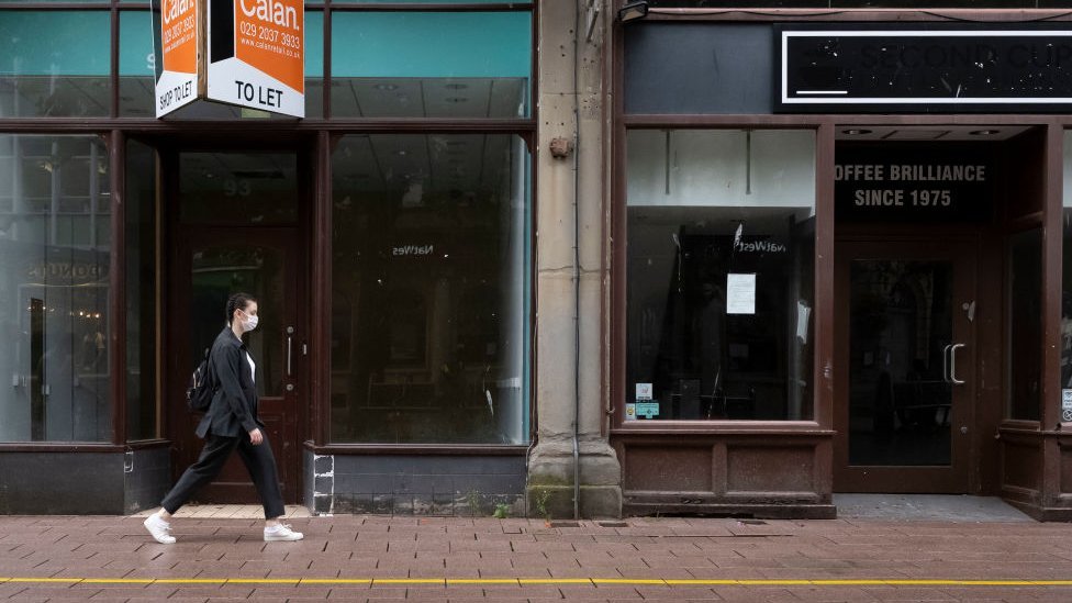 Женщина идет по улице Кардиффа с пустыми магазинами позади
