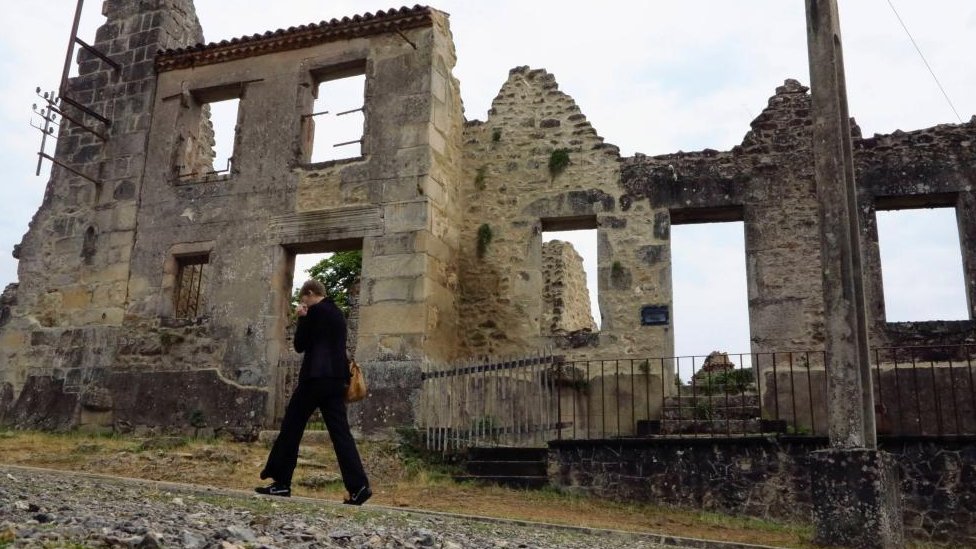 A person walks past abandoned buildings in the French town of Oradour-sur-Glane
