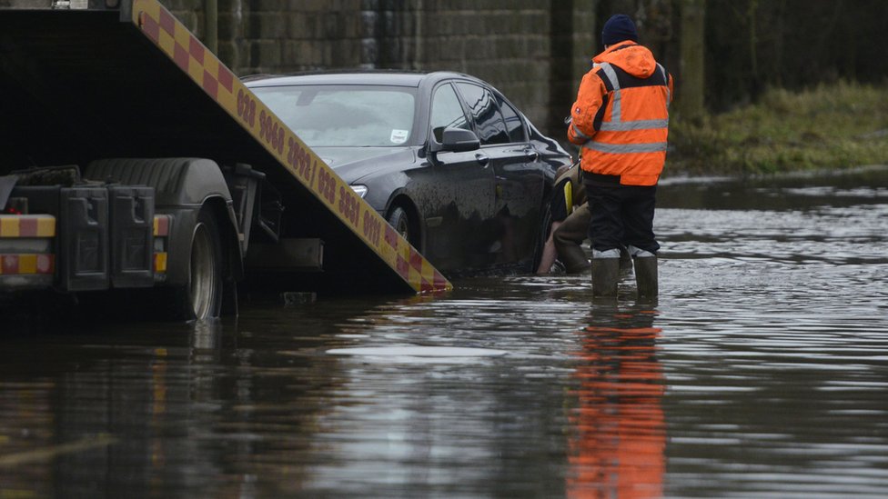 Персонал по эвакуации автомобилей занимается устранением автомобиля, застрявшего на дороге, пострадавшей от наводнения