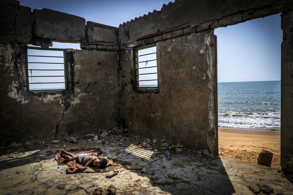 Un niño duerme dentro de una casa en ruinas en una playa en Ghana en 2019