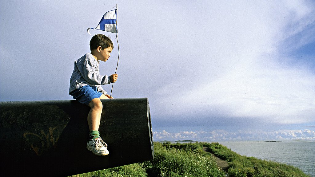 Niño con bandera de Finlandia sentado en un cañon