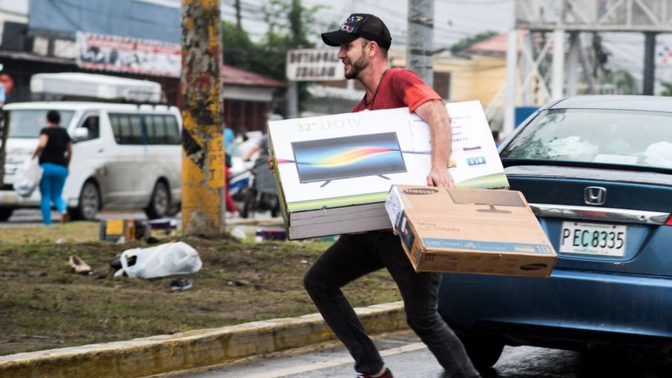 Las protestas pacíficas derivaron en violencia y saqueos. Un hombre transporta una televisión.