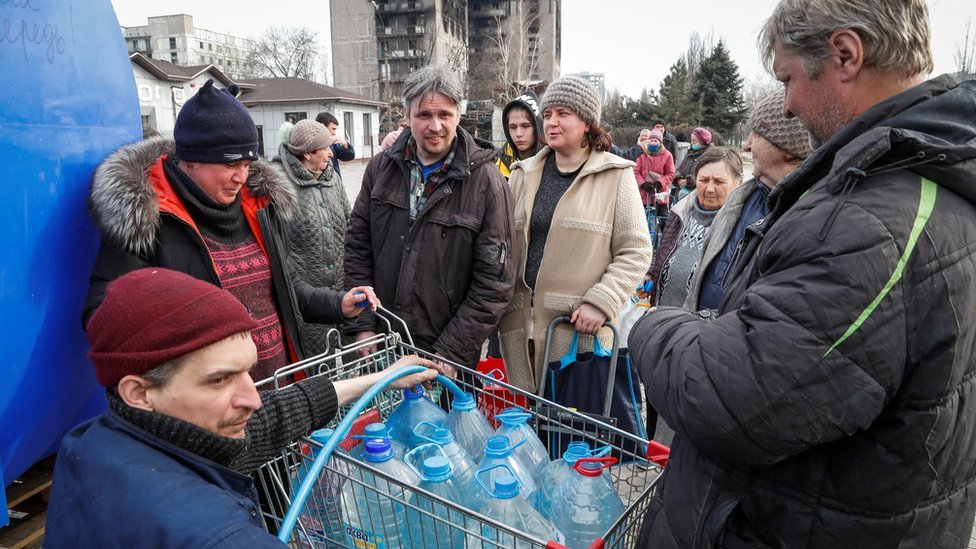 People queuing around a supermarket trolley containing bottled water