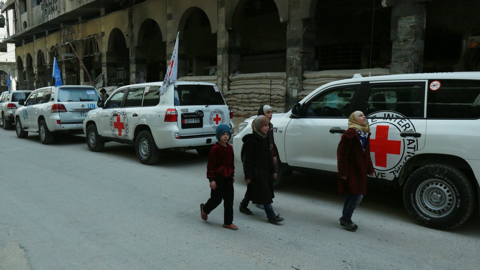 Сирийские дети проходят мимо автомобилей ООН и Международного комитета Красного Креста (МККК), доставляющих гуманитарную помощь в сирийский город Дума