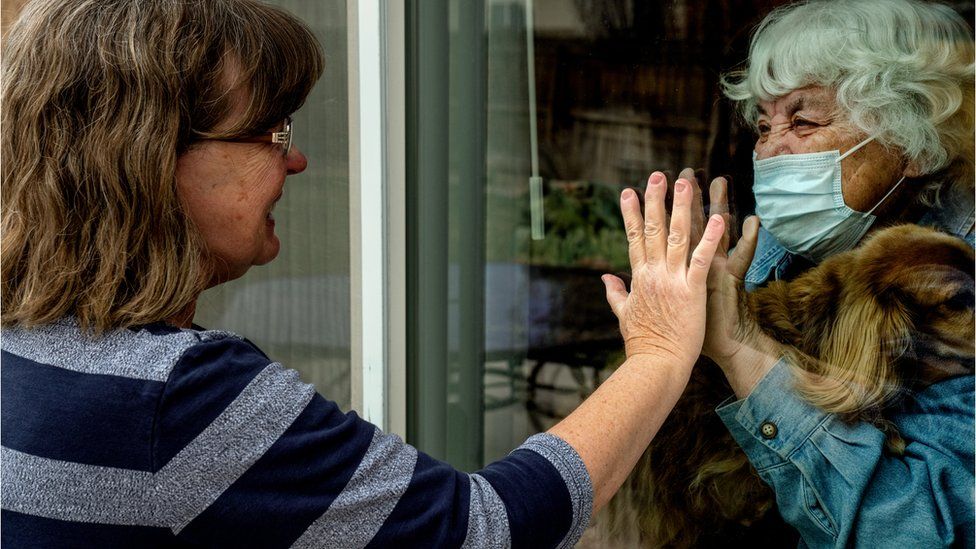 Dos mujeres separadas por un vidrio se saludan