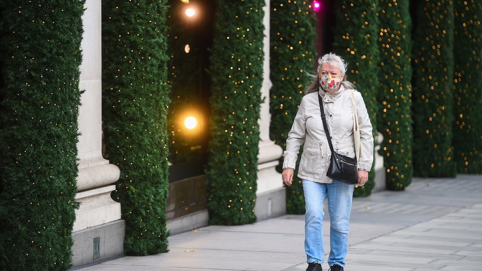 A woman wearing a face mask passes Christmas lights outside shops on Oxford Street, London