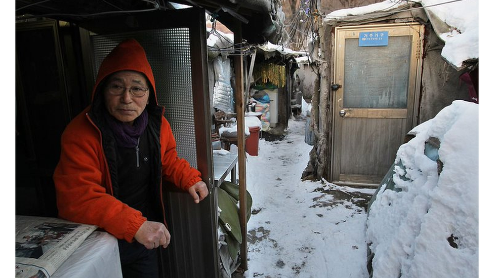 Un hombre mayor de Corea del Sur se sienta en el barrio pobre de Guryong en Seúl con nieve en el suelo.