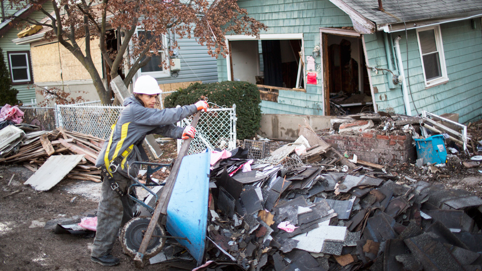 Hombre sacando escombros con una carretilla frente a una casa destruida tras el huracán Sandy