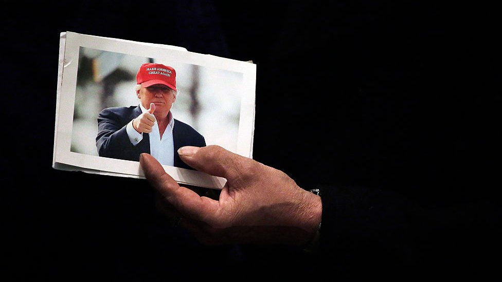 Мужчина держит фотографию кандидата в президенты от республиканской партии Дональда Трампа у канатной дороги во время предвыборной кампании в Конгресс-центре сотовой связи США 1 февраля 2016 года в Сидар-Рапидс, штат Айова.