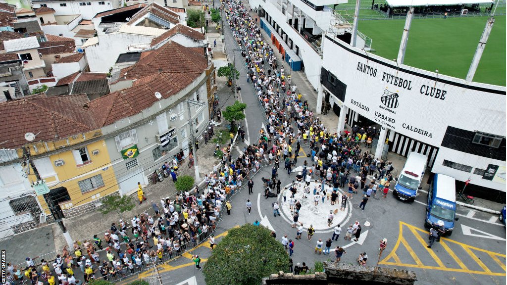 Mourners stand in line outside Vila Belmiro stadium as they wait to pay their respects to Pele