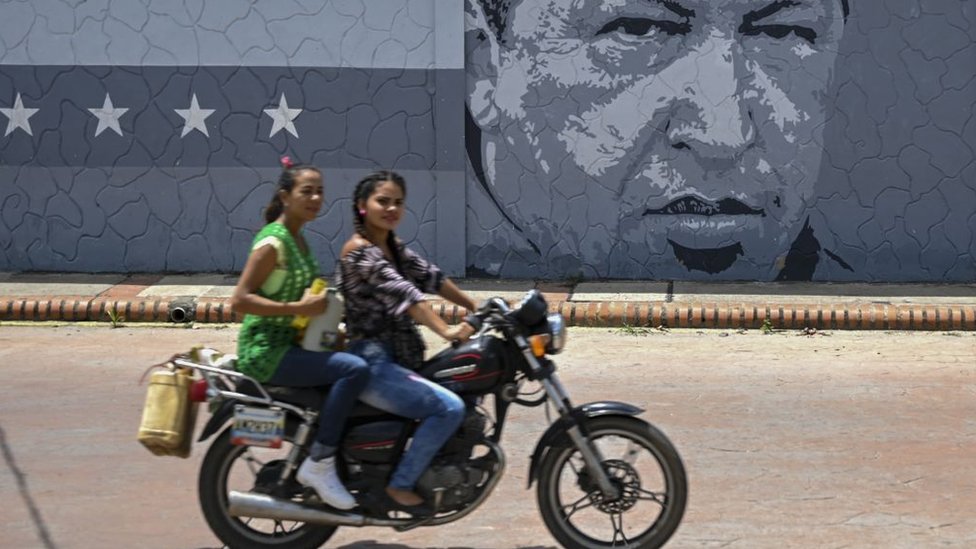 Dos mujeres pasan en moto junto a un mural con el rostro de Hugo Chávez en Barinas.