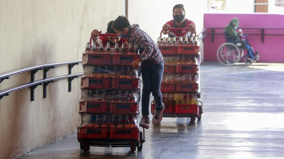 Рабочие несут газированные напитки в защитных масках 9 мая 2020 года в Керетаро, Мексика.