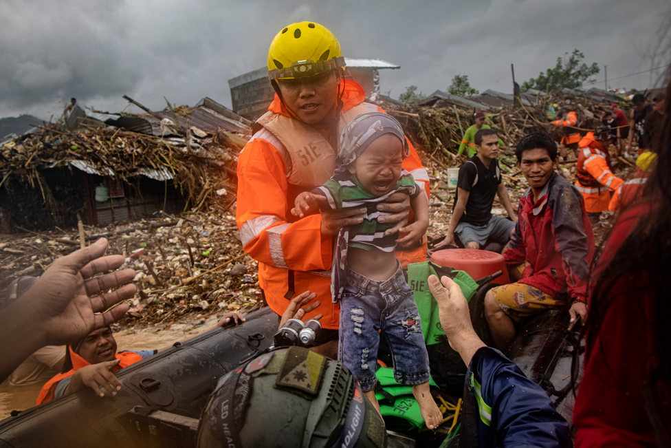 A rescuer carries a baby as floodwaters rise in a submerged village