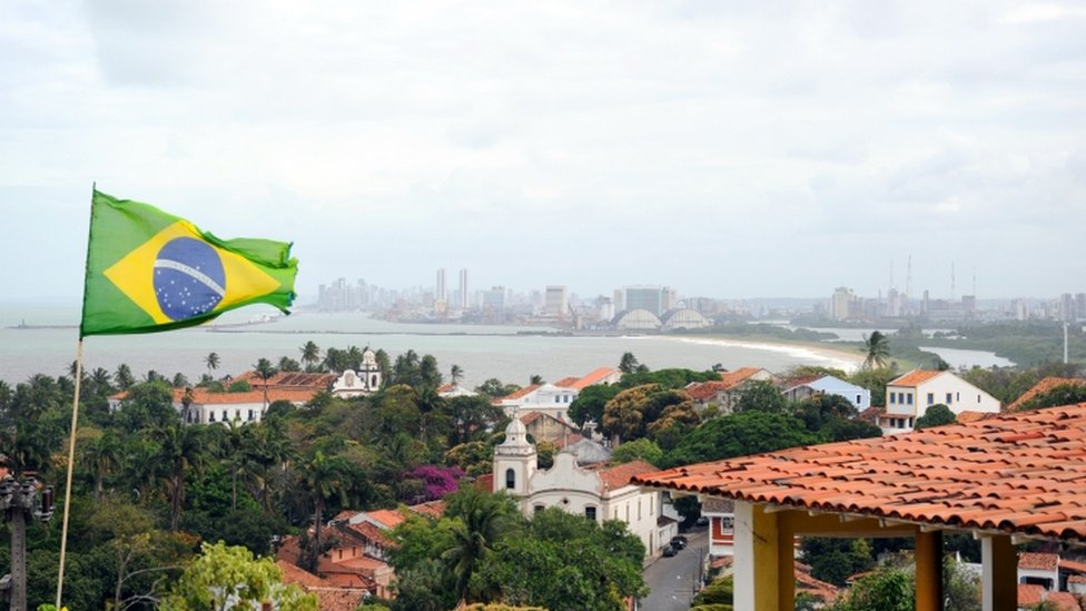 Бразильский флаг, развевающийся над домом на берегу Ресифи, на заднем плане в северо-восточном бразильском городе Олинда в штате Пернамбуку, сентябрь 2010 года.
