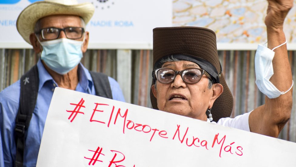 Dos personas con una pancarta que dice Mozote unca mas.