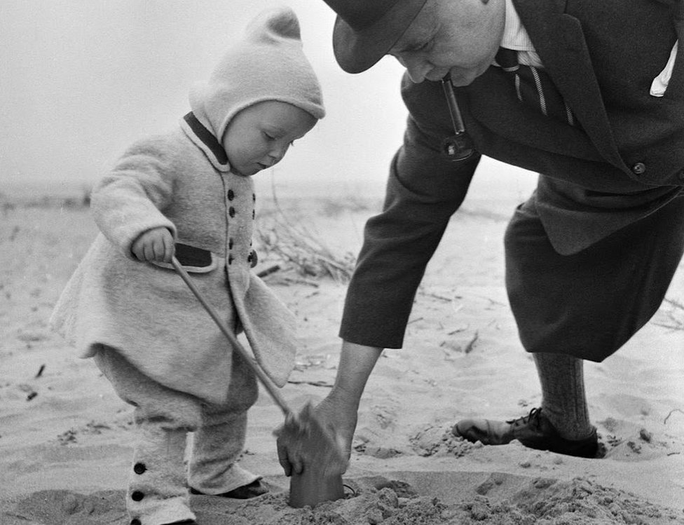 мужчина помогает ребенку построить замок из песка