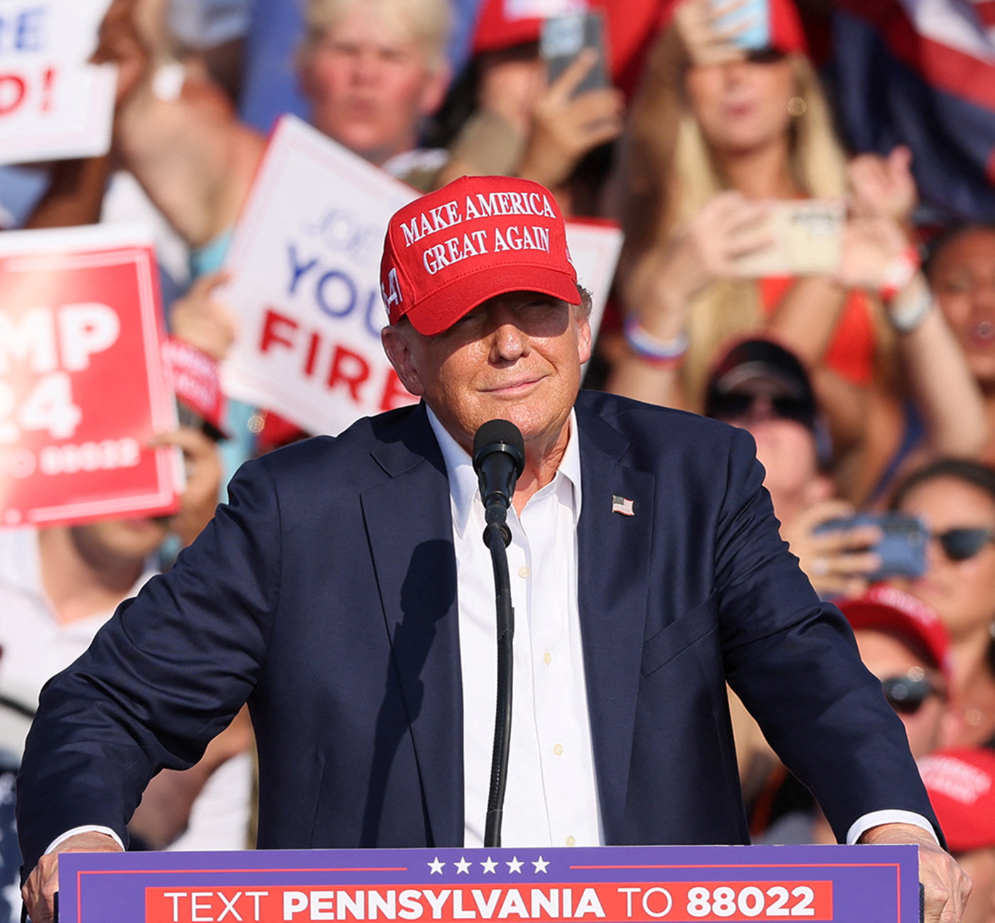 Trump speaking at lectern wearing baseball cap