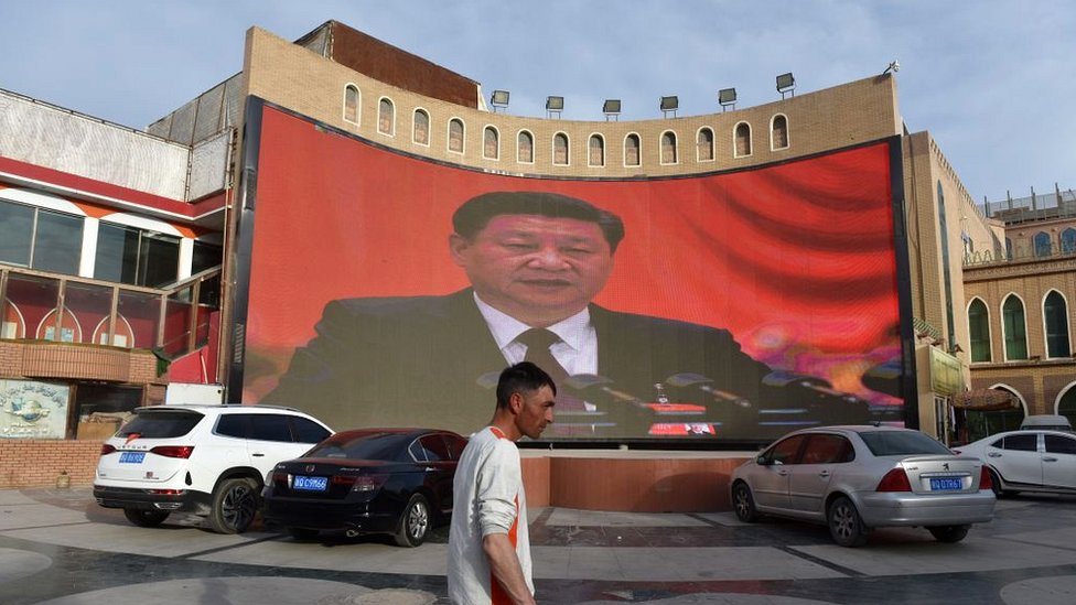 Мужчина проходит мимо экрана с изображениями президента Китая Си Цзиньпина в Кашгаре в северо-западном регионе Китая Синьцзян