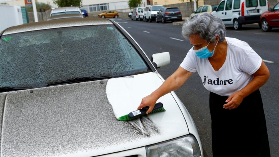 A woman cleans the ashes from her car on La Palma.
