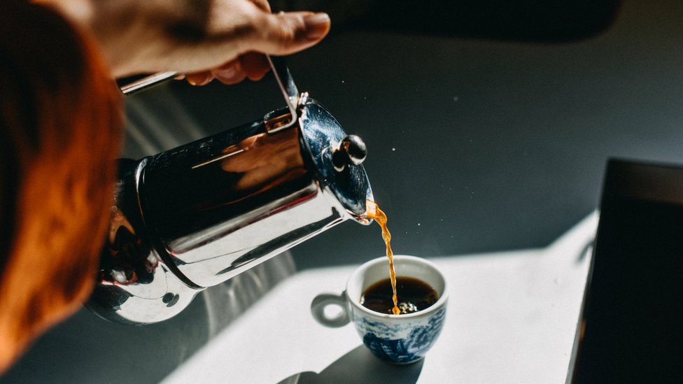 Foto de uma pessoa servindo uma xícara de café expresso em uma xícara pequena