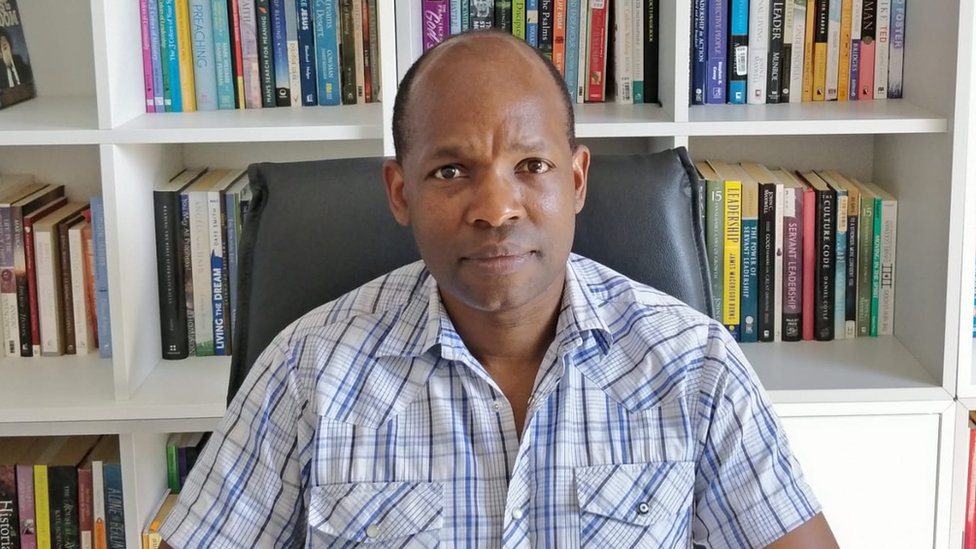 Dr Nyarie Sithole sitting at desk in front of a bookshelf.
