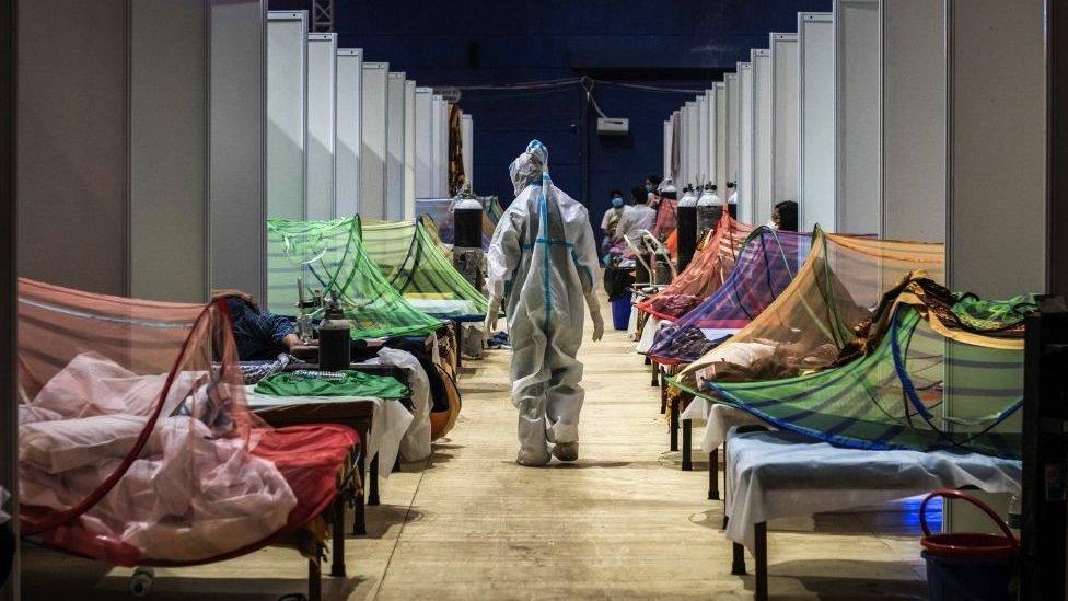 新德里英聯邦運動會村體育場內的臨時護理設施內，一名身穿個人防護裝備的醫務人員正在觀察感染新冠的患者（2021年5月2日）
