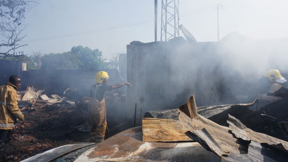 Firefighters work next to burnt wreckages after a fuel tanker explosion in Freetown, on November 6, 2021