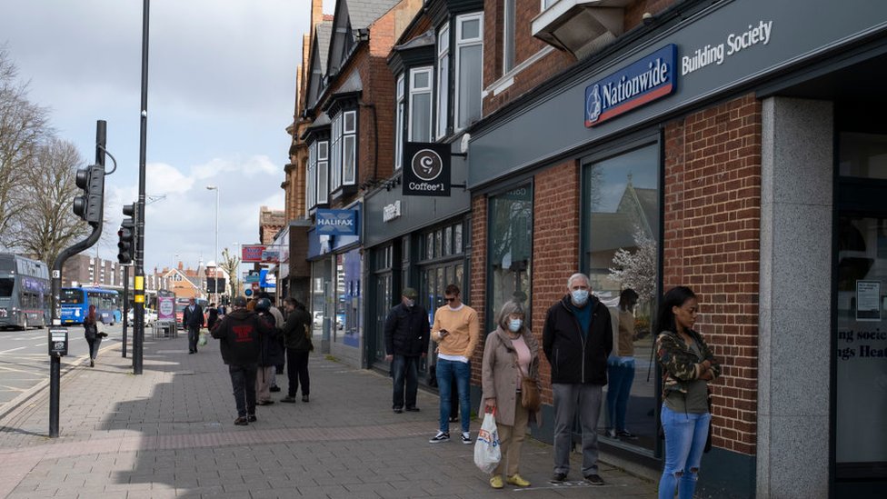 People wearing masks queue outside a Nationwide bank