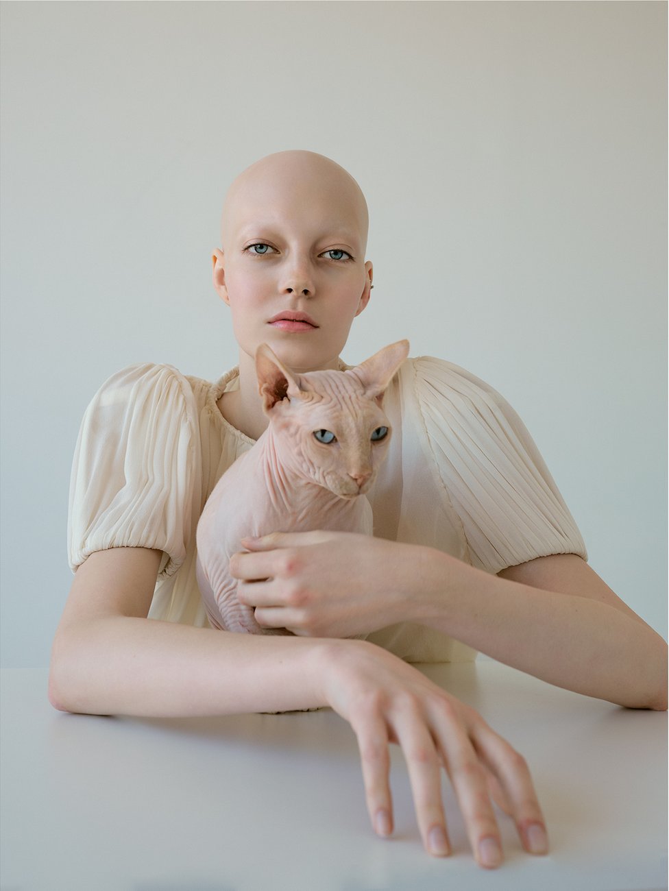 A young woman without hair holds a bald cat