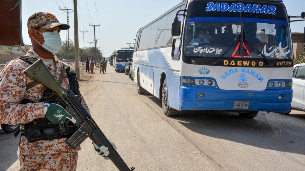 An armed Pakistani soldier stands guard as a bus carrying pilgrims returning from Iran are driven to a quarantine area, March 2020