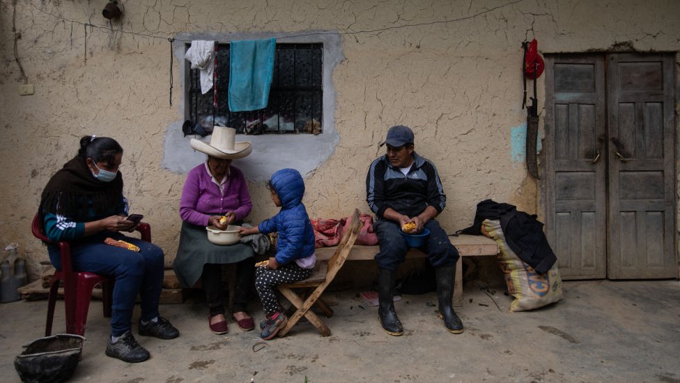 Una familia en Cajamarca está a las afueras de una casa rústica desgranando maíz.