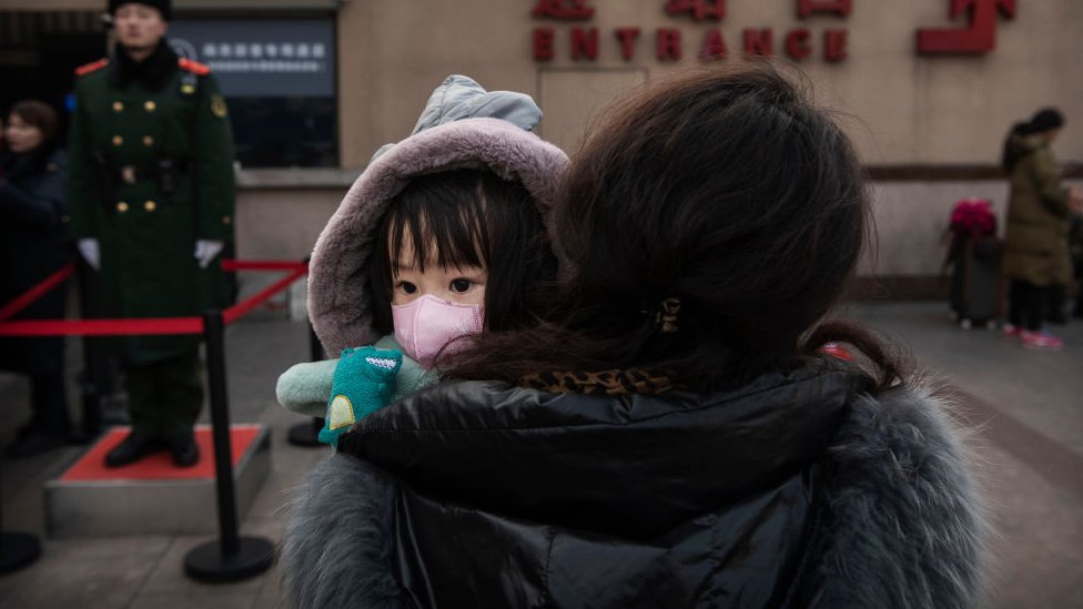 Китайская девушка носит защитный в маске, когда ее держит родственник в ожидании посадки в поезд на Пекинской железной дороге