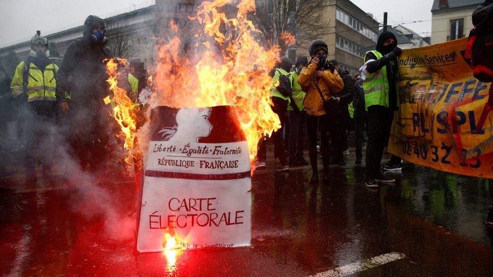 Protesters wearing yellow vests stand near a burning facsimile voter registration card during a demonstration by the "yellow vests" movement in Nantes, France, 15 December.