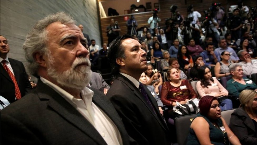 Заместитель министра по правам человека Алехандро Энсинас Родригес (слева) и губернатор штата Веракрус Куитлауак Гарсия Хименес (справа) смотрят экран, на котором публично извиняются перед родственниками пяти молодых людей, убитых в 2016 году
